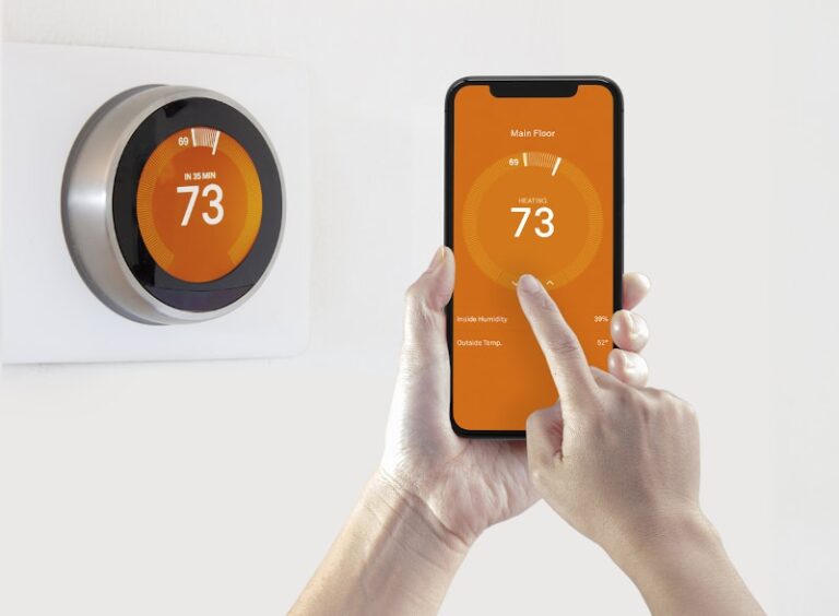 orange smart thermostat behind phone displaying thermostat app